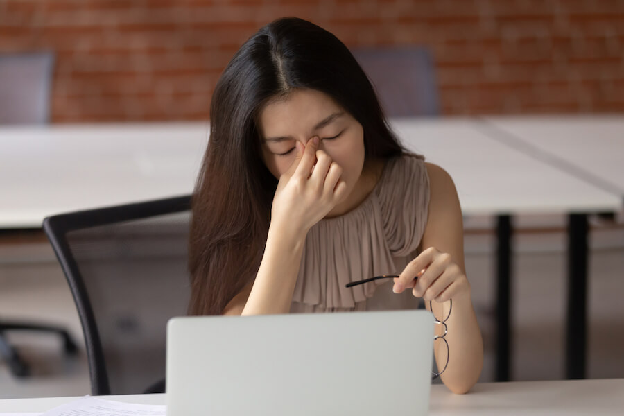 Woman rubbing her eyes in front of a laptop computer