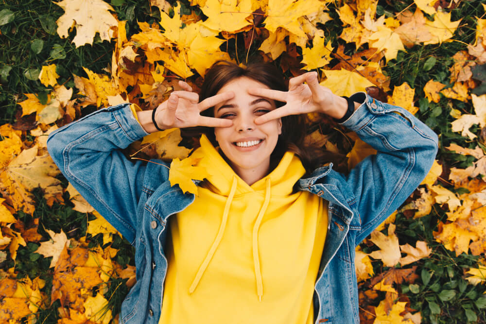 Woman laying down outside surrounded by yellow leaves